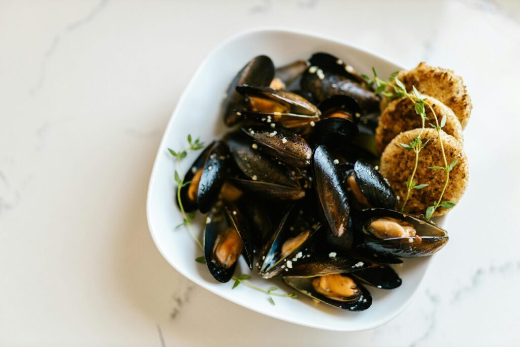 A delectable seafood dish of mussels served in a white bowl with crackers.