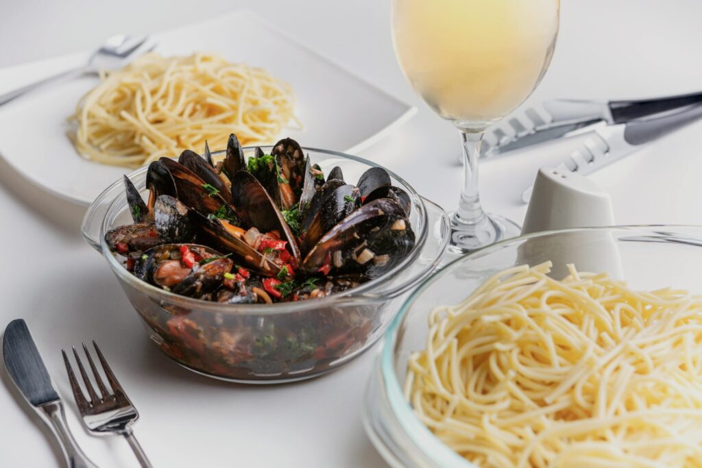 A delectable seafood pasta dish featuring fresh mussels complemented by a glass of white wine.