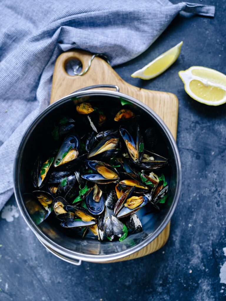 Top view of a pot filled with steamed mussels, garnished with fresh herbs and served with lemon wedges.